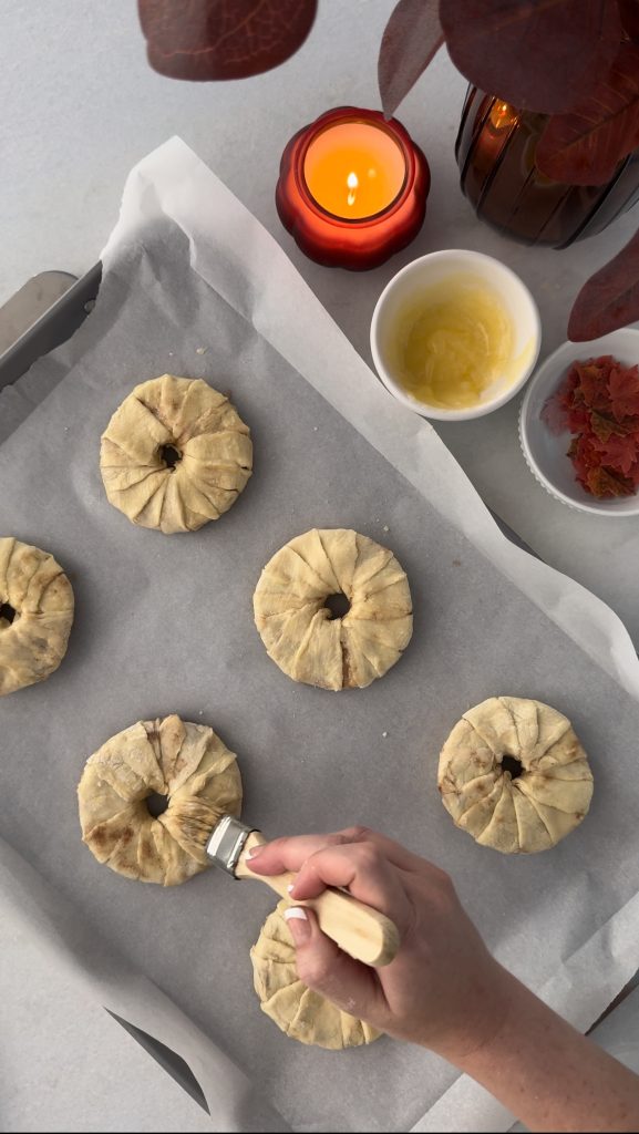 These Apple Cinnamon Pastry Donuts are filled with fresh apple slices, surrounded by puff pastry, covered in cinnamon sugar, drizzled with caramel sauce, and topped with a cinnamon stick and edible maple leaf.