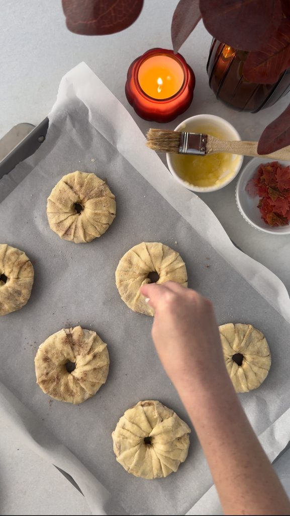 These Apple Cinnamon Pastry Donuts are filled with fresh apple slices, surrounded by puff pastry, covered in cinnamon sugar, drizzled with caramel sauce, and topped with a cinnamon stick and edible maple leaf.