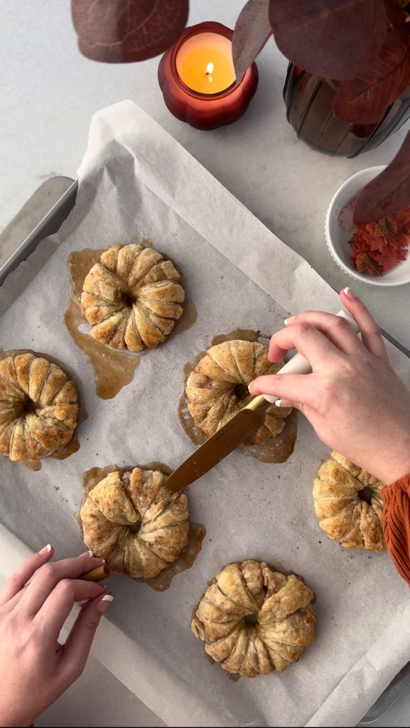 These Apple Cinnamon Pastry Donuts are filled with fresh apple slices, surrounded by puff pastry, covered in cinnamon sugar, drizzled with caramel sauce, and topped with a cinnamon stick and edible maple leaf.