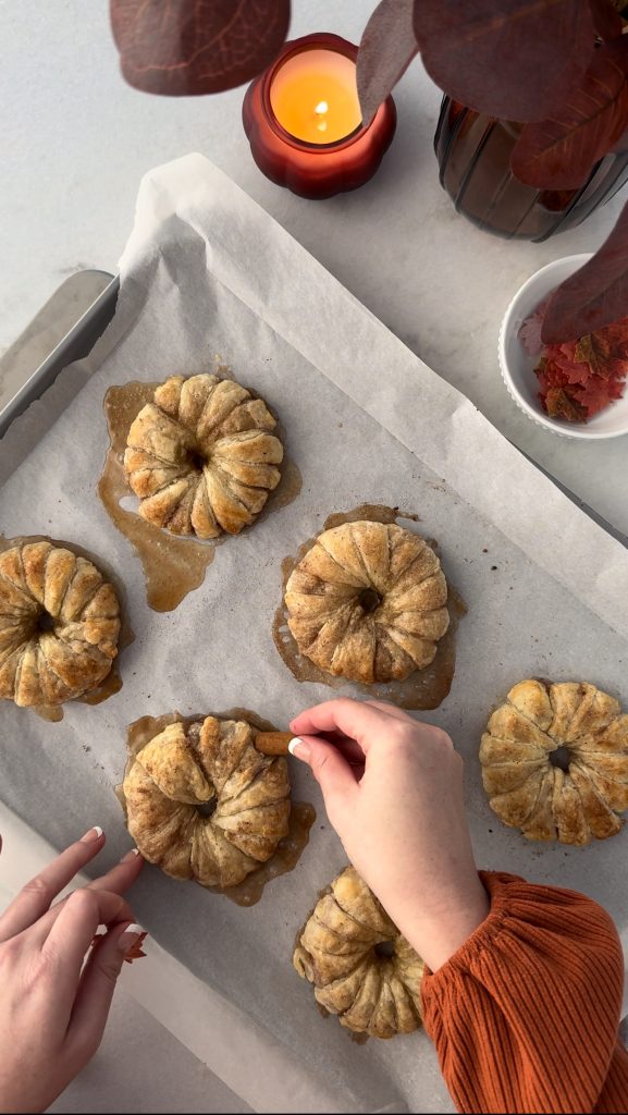 These Apple Cinnamon Pastry Donuts are filled with fresh apple slices, surrounded by puff pastry, covered in cinnamon sugar, drizzled with caramel sauce, and topped with a cinnamon stick and edible maple leaf.
