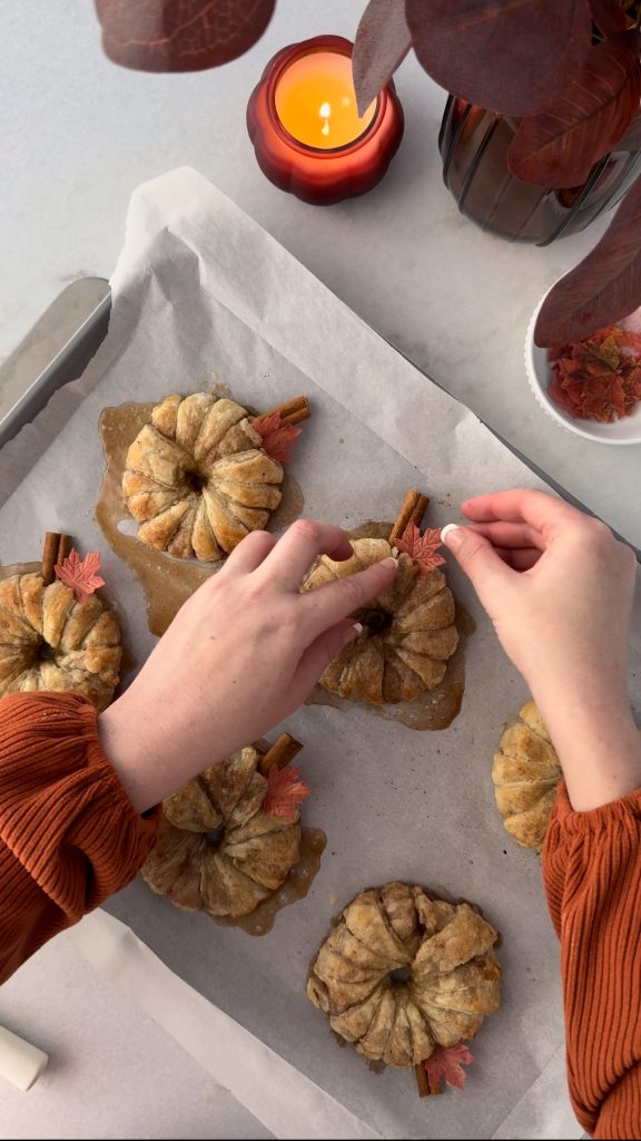 These Apple Cinnamon Pastry Donuts are filled with fresh apple slices, surrounded by puff pastry, covered in cinnamon sugar, drizzled with caramel sauce, and topped with a cinnamon stick and edible maple leaf.