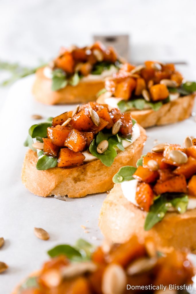 This Whipped Goat Cheese Butternut Squash Bruschetta begins with sliced toasted baguette, topped with whipped goat cheese, arugula, roasted butternut squash, honey, and pumpkin seeds.  