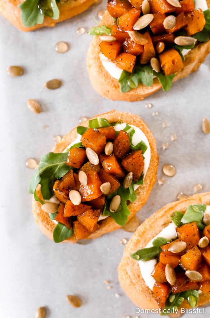 This Whipped Goat Cheese Butternut Squash Bruschetta begins with sliced toasted baguette, topped with whipped goat cheese, arugula, roasted butternut squash, honey, and pumpkin seeds.  