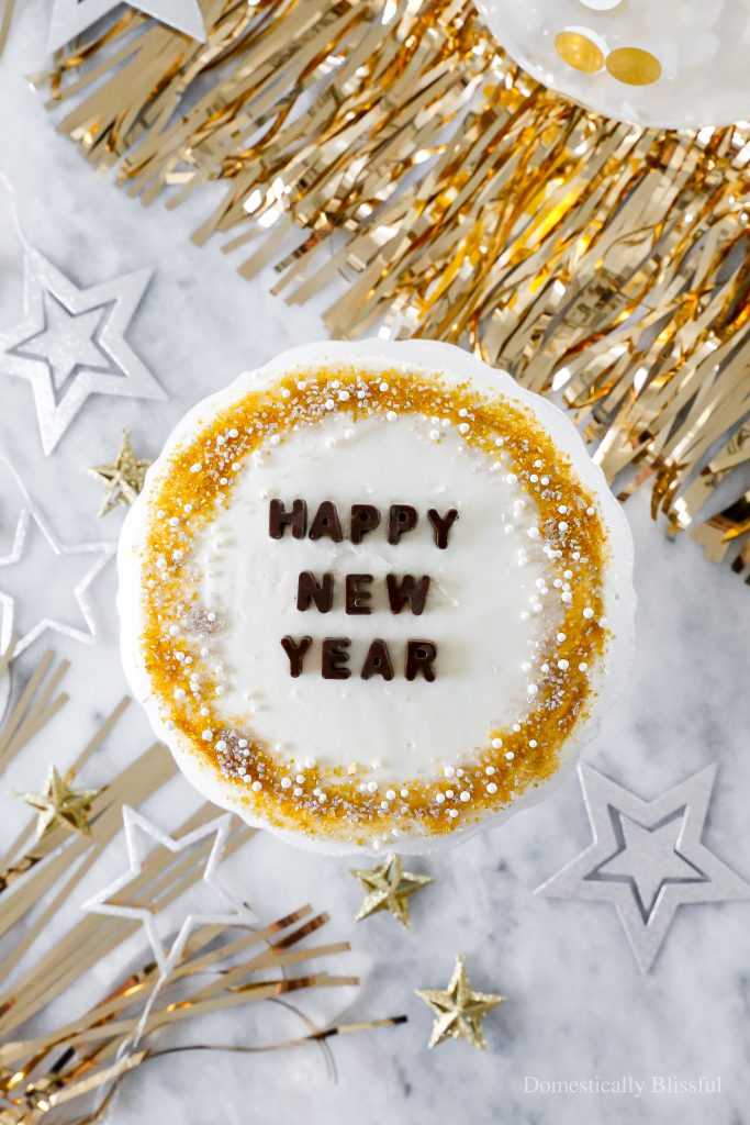 A quick and easy DIY Happy New Year's Eve Cake using a store-bought cake and redecorating it with gold, silver, and white sprinkles and chocolate letters.