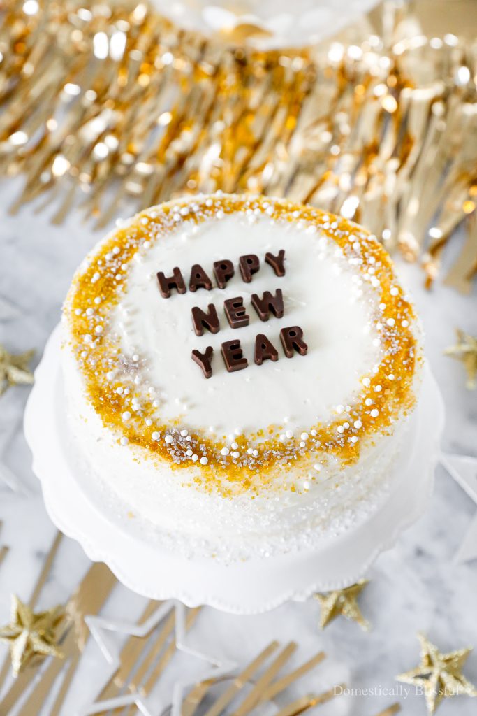 A quick and easy DIY Happy New Year's Eve Cake using a store-bought cake and redecorating it with gold, silver, and white sprinkles and chocolate letters.