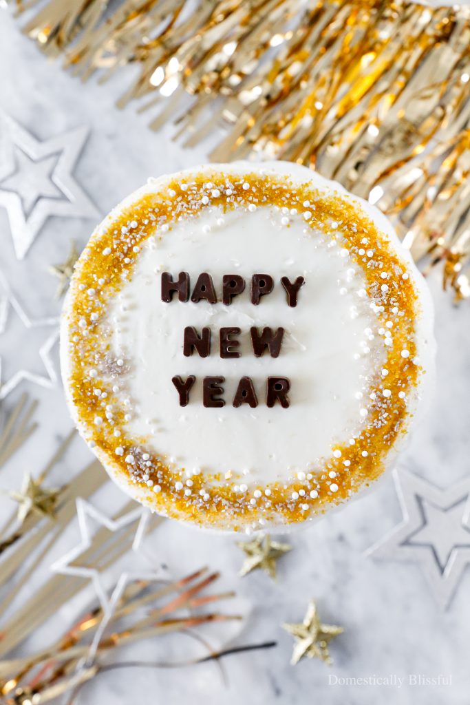 A quick and easy DIY Happy New Year's Eve Cake using a store-bought cake and redecorating it with gold, silver, and white sprinkles and chocolate letters.