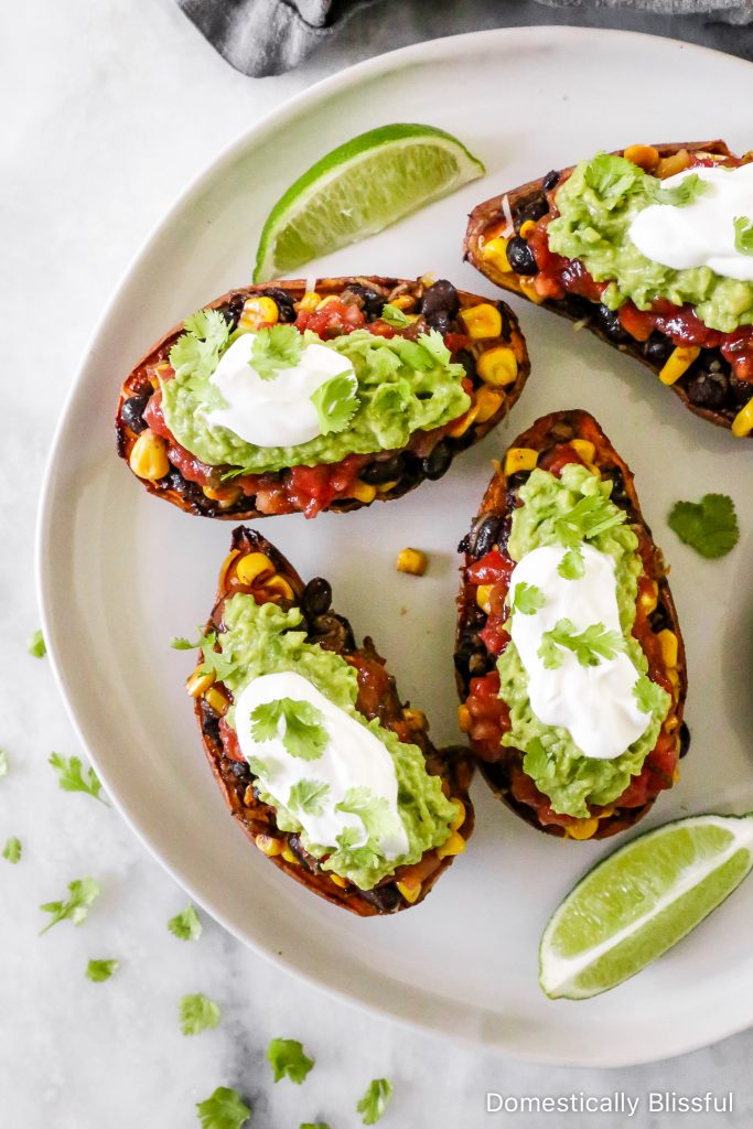 These Loaded Black Bean Taco Sweet Potatoes are covered in seasoned black beans and corn and topped with cheese, sour cream, salsa, guacamole, cilantro, and a squeeze of lime.