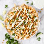 These Mexican Street Corn Fries are super easy to make with a base of crispy fries and melted cheese, topped with roasted corn, drizzled with cilantro cream sauce, and a squeeze of lime.