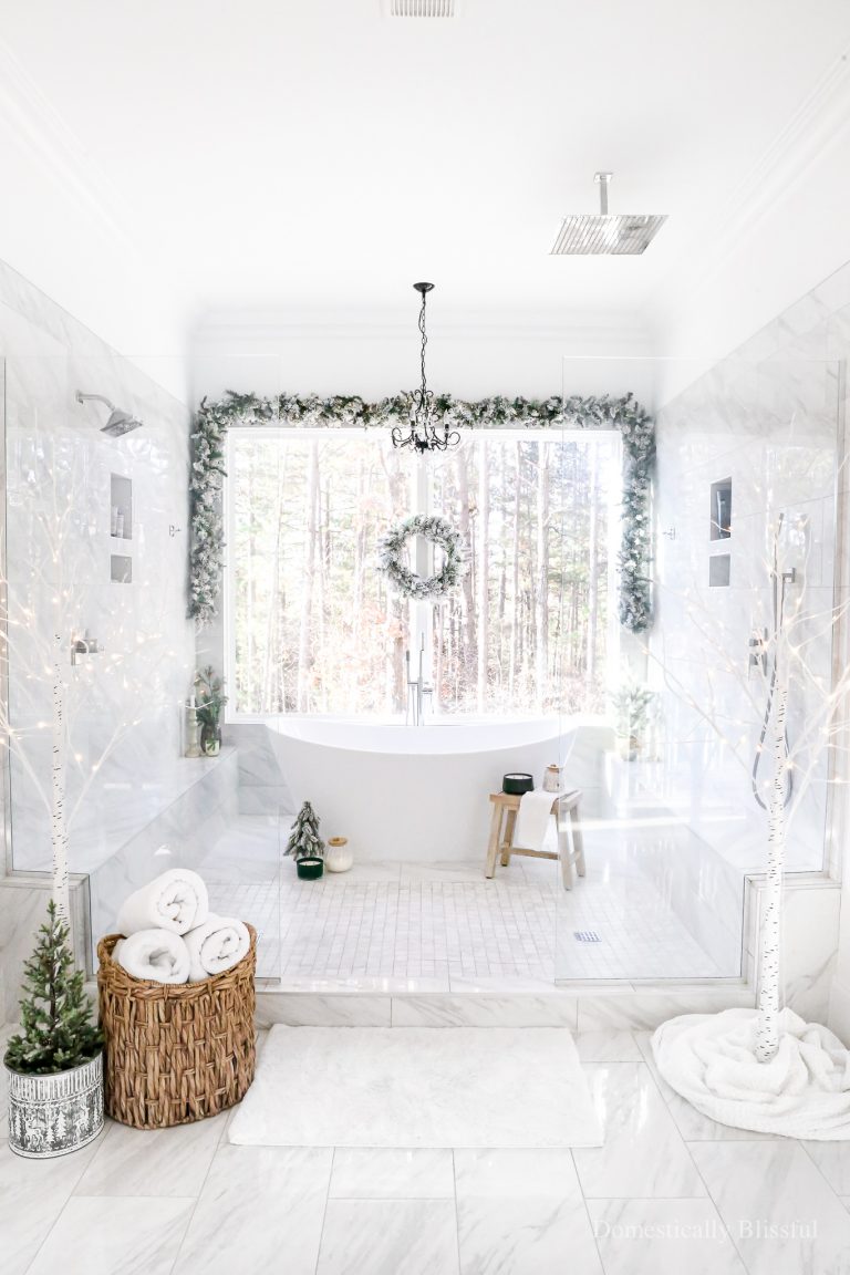 Snowy Bathroom Christmas Decor with flocked garland, a flocked wreath, lit birch trees, and little Christmas trees.